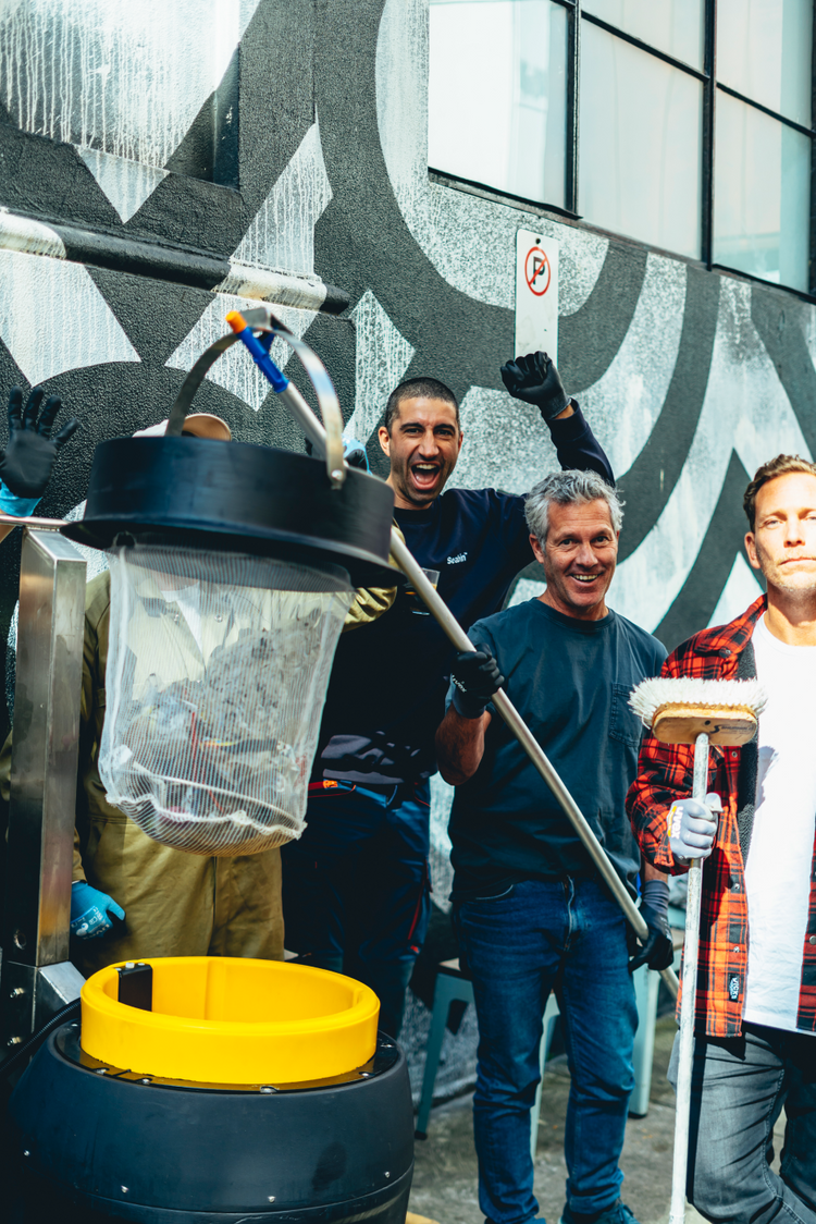 Three men participating in a community clean-up event with trash collection equipment.